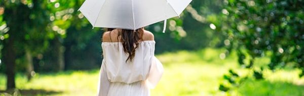 Een vrouw die tijdens warm weer met een parasol loopt omdat ze last heeft van jeukende huid